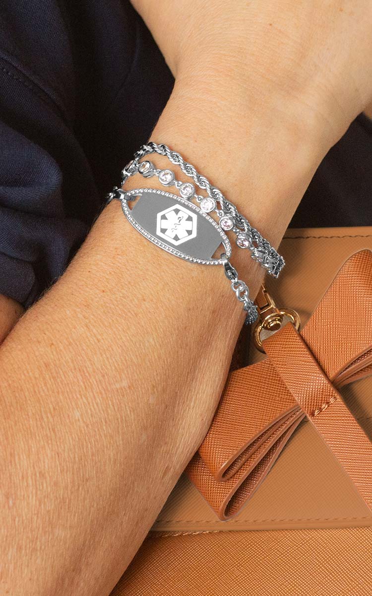 Woman with hand on book wearing silver tennis bracelet with mother of pearl medical ID tag