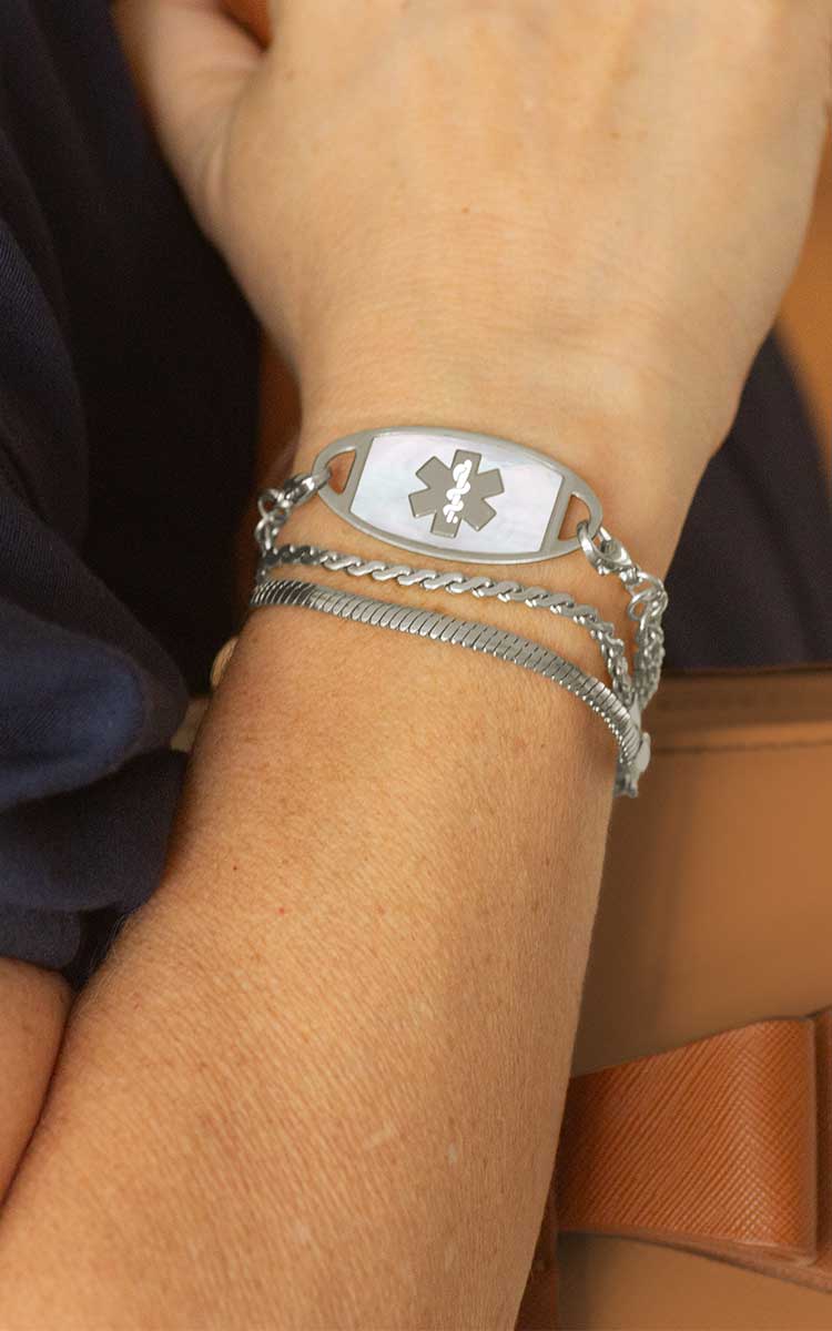 Woman with hand on book wearing silver tennis bracelet with mother of pearl medical ID tag