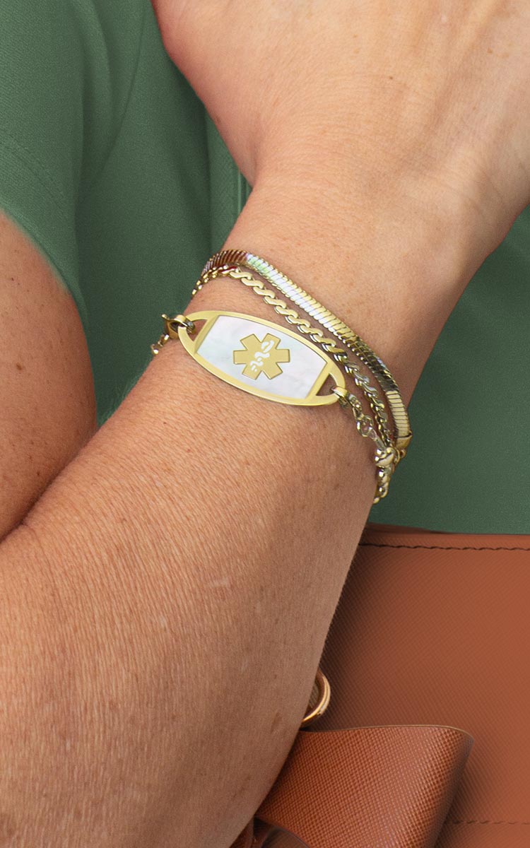 Woman with hand on book wearing silver tennis bracelet with mother of pearl medical ID tag