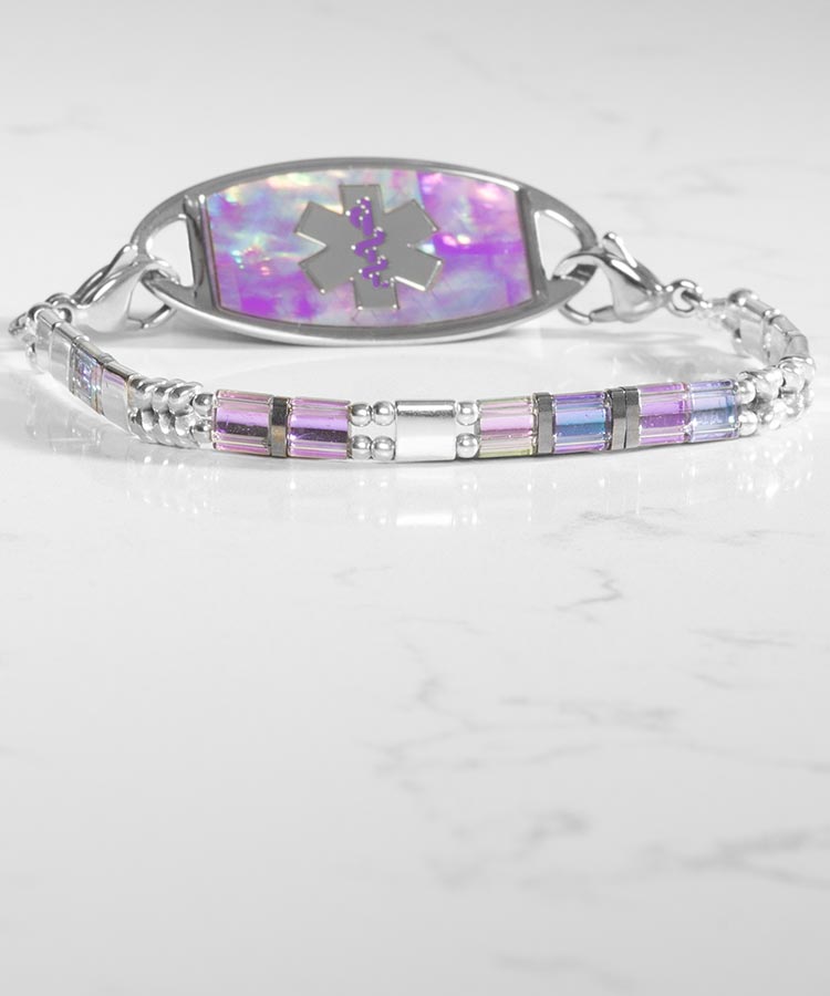 Woman with hand on book wearing silver tennis bracelet with mother of pearl medical ID tag