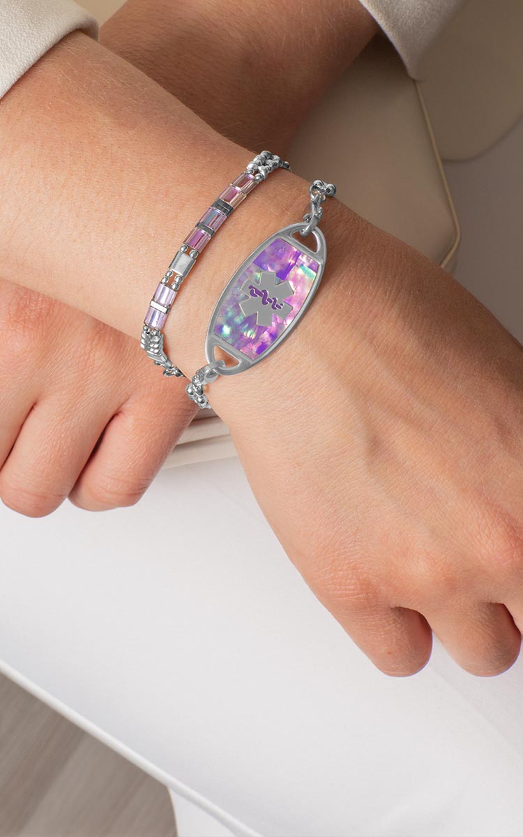 Woman with hand on book wearing silver tennis bracelet with mother of pearl medical ID tag