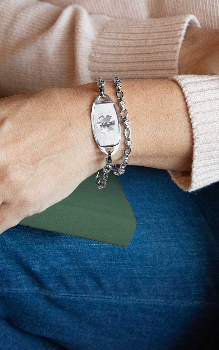 Woman with hand on book wearing silver tennis bracelet with mother of pearl medical ID tag
