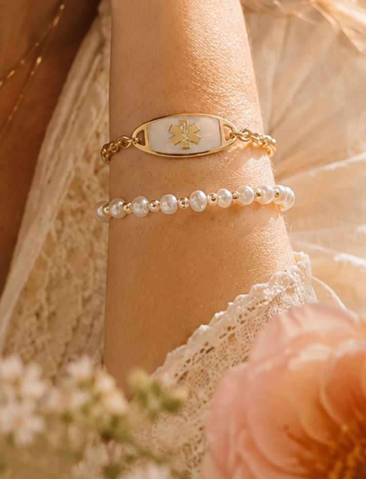 Woman with hand on book wearing silver tennis bracelet with mother of pearl medical ID tag