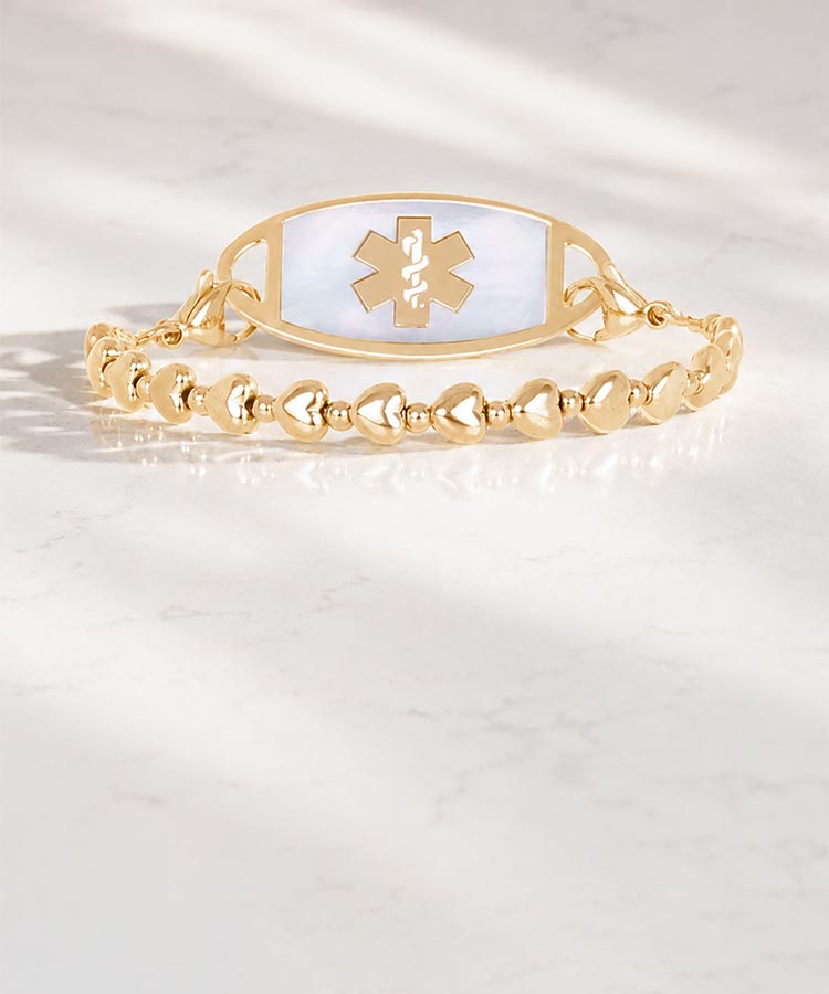 Woman with hand on book wearing silver tennis bracelet with mother of pearl medical ID tag