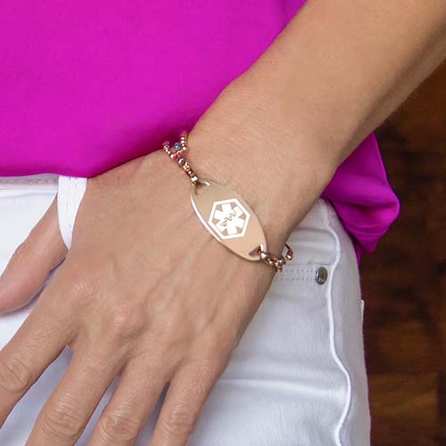 Woman wearing the Rose Gold Tone Oval Medical ID Tag, a water-resistant rose plated stainless med ID tag, on an LH bracelet