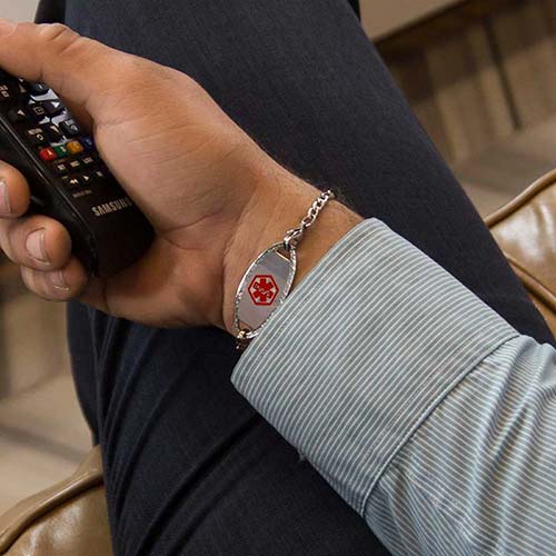 Man holding TV remote wearing a LH bracelet with the Oval Border Medical ID Tag, a stainless tag with rope detail on the edge