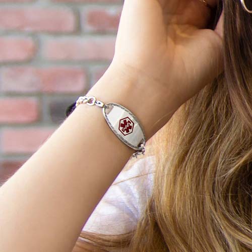 Woman holding tennis racquet wearing a LH bracelet with Oval Border Medical ID Tag, a stainless tag with rope-detail edges