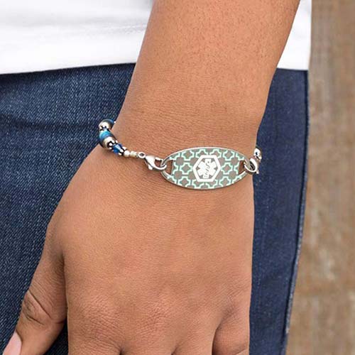 Woman wearing the Turquoise Silhouette Medical ID Tag with geometric background pattern and turquoise inlay on an LH bracelet
