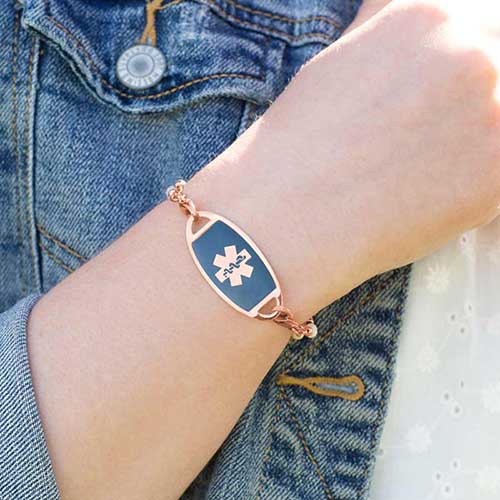 Woman in denim jacket wearing rose gold tone stainless steel medical ID tag with sapphire blue inlay and coordinating rose gold tone medical symbol.