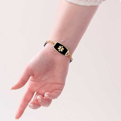 Woman wearing gold medical ID bracelet with black enamel medical alert tag