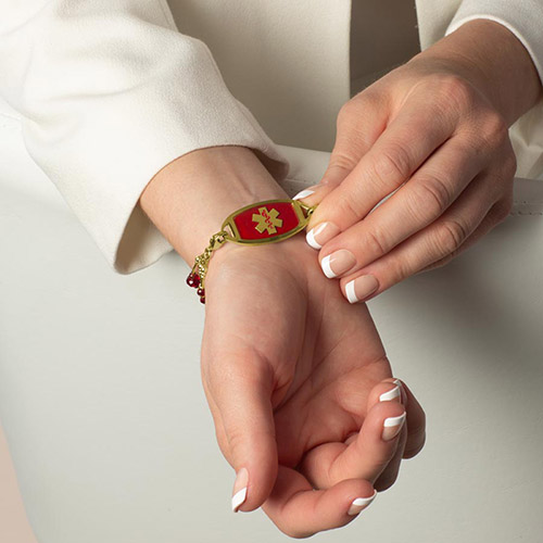 Icon Flat Medical Alert Tag in Crimson Watercolor with a gold caduceus symbol, shown on a wrist with Lauren’s Hope interchangeable bracelet strand