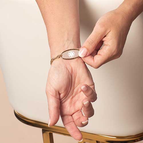 Person displaying a decorative, rose gold tone, stainless steel medical ID tag with white medical alert symbol.