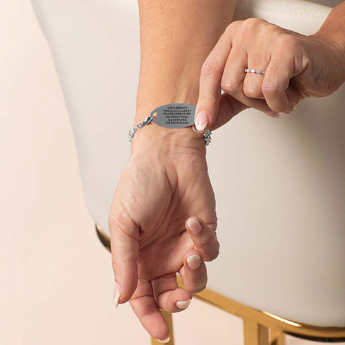Woman wearing silver bracelet with custom-engraved Icon CZ Silver tag, pointing to medical info on the back.