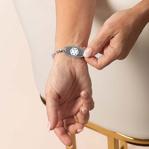 Woman displaying front of silver bracelet with mother-of-pearl medical tag and silver caduceus symbol.