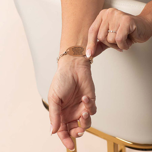 Woman wearing bracelet in rose gold, pointing to engraved medical tag with personal information.