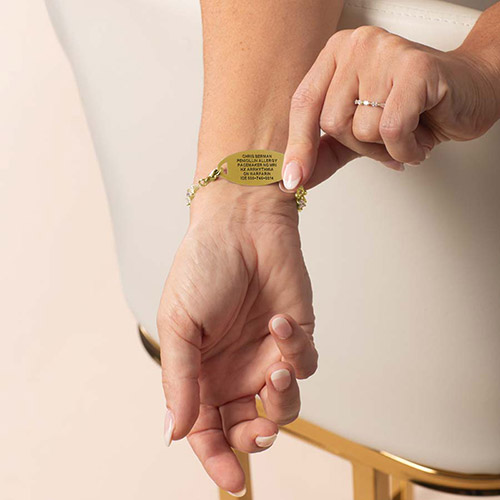 Woman wearing bracelet in gold, pointing to engraved medical ID tag.