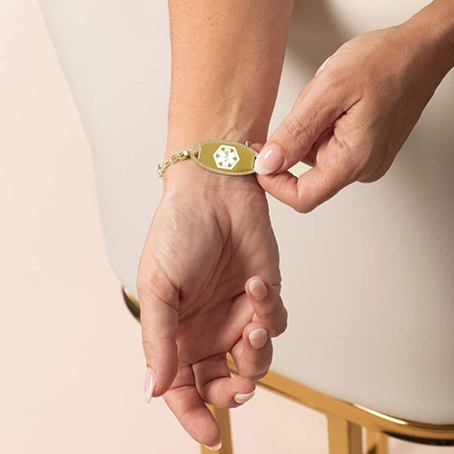 Front-facing view of gold bracelet on model, featuring Icon CZ Gold tag with bright caduceus symbol.