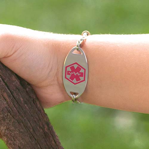 Little boy holding rustic hiking stick, wearing stretch medical ID bracelet with alert tag facing forward with red caduceus.