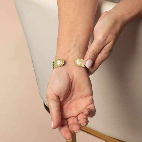 Model wearing a gold-tone medical ID cuff, showing the open back with medical symbols engraved on both ends.
