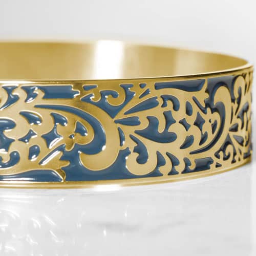 Close-up of a gold-tone medical ID cuff featuring an intricate filigree pattern with blue accents.