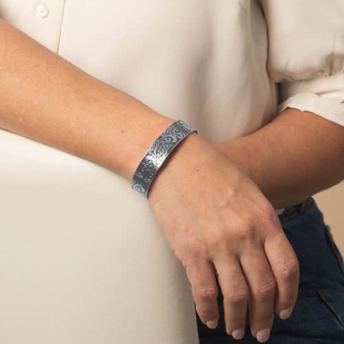 Model wearing a silver-tone cuff bracelet featuring an intricate filigree design with blue inlay.
