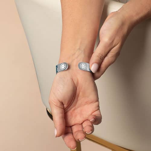 Model wearing a silver-tone medical ID cuff with blue filigree detailing, showing medical symbols on each end.