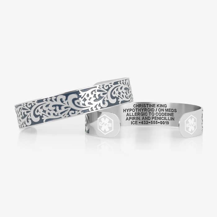 Silver-tone medical ID cuff shown front and back, featuring blue filigree detailing, medical symbols, and custom engraving.