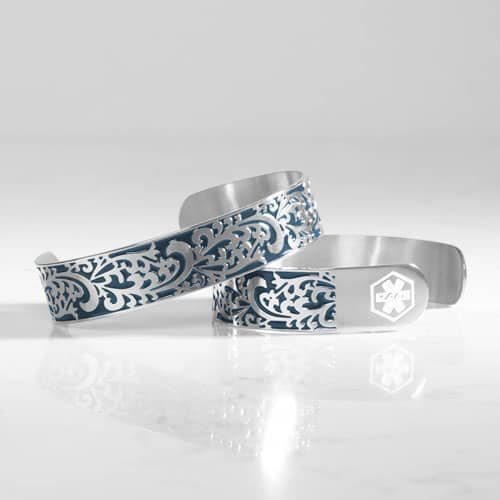 Two silver-tone cuff bracelets featuring intricate filigree designs with blue inlay, one displaying a medical symbol.