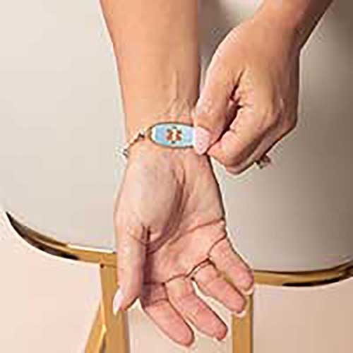 Woman showing blue mother of pearl inlaid rose gold medical ID tag on beaded bracelet