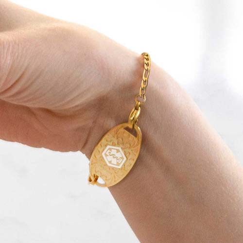 Woman wearing gold tone medical alert tag with decorative inlay and white caduceus