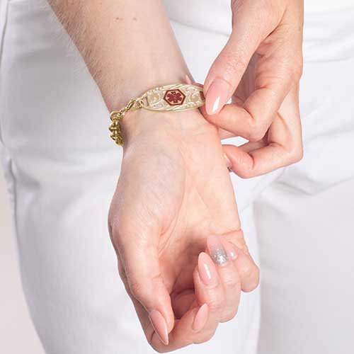 Woman showing gold tone stainless steel medical ID tag with decorative filigree pattern and red medical symbol.
