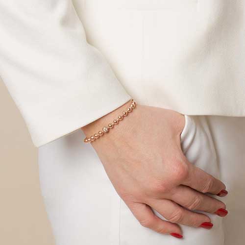 Woman with thumb in pocket wearing rose gold beaded medical ID bracelet