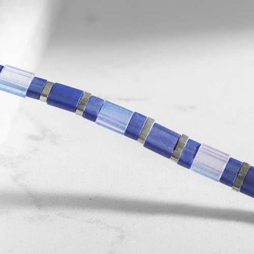 Close-up of a blue and silver tile-style medical ID bracelet chain, highlighting geometric beads with modern color-block detailing.