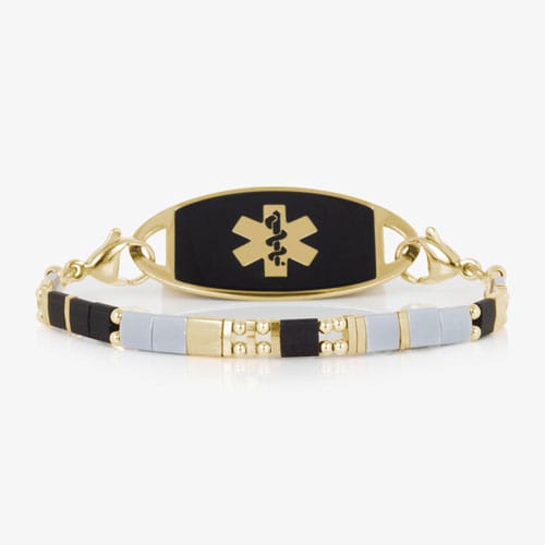 Gold-tone medical ID bracelet with a black ID tag and a strand of black, light gray, and gold-tone rectangular beads.