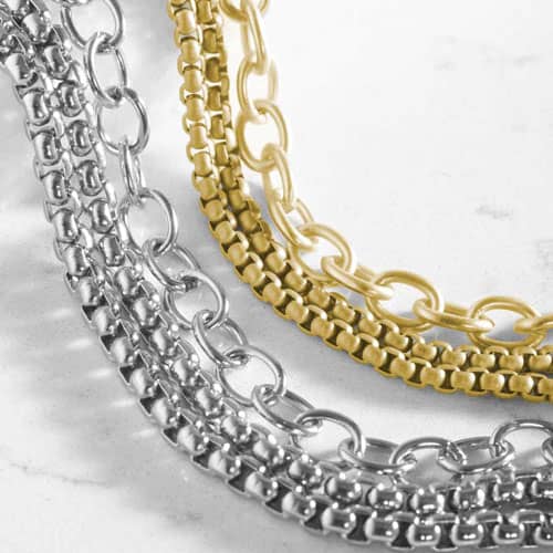 Close-up of silver-tone and gold-tone layered bracelet designs featuring mixed chain textures and oval link accents.