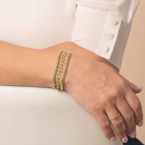 Model wears a gold-tone layered medical ID bracelet with mixed chain textures and an oval mother-of-pearl ID tag.