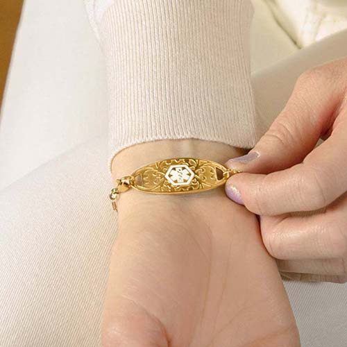 Woman showing gold medical alert tag with decorative inlay and white medical caduceus symbol