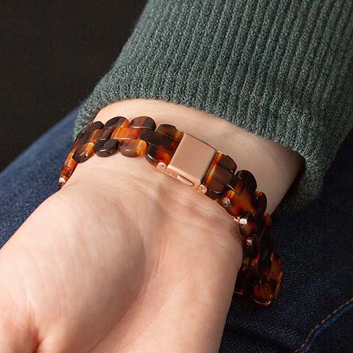 Woman wearing green sweater closing rose gold clasp on medical ID bracelet with tortoiseshell resin band.