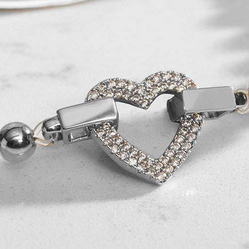 Close-up of the silver heart-shaped centerpiece, fully paved with small, sparkling clear crystals, showing connection points to the beaded strand on either side.