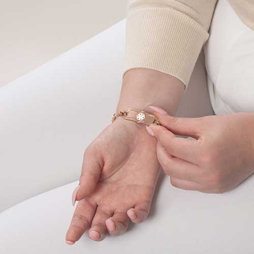 Woman showing rose gold medical ID alert tag with white medical symbol