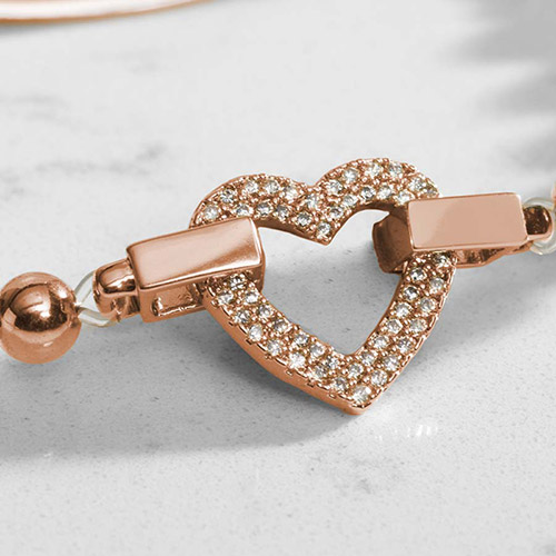Close-up of the rose gold heart-shaped centerpiece, fully paved with small, sparkling clear crystals, showing connection points to the beaded strand on either side.