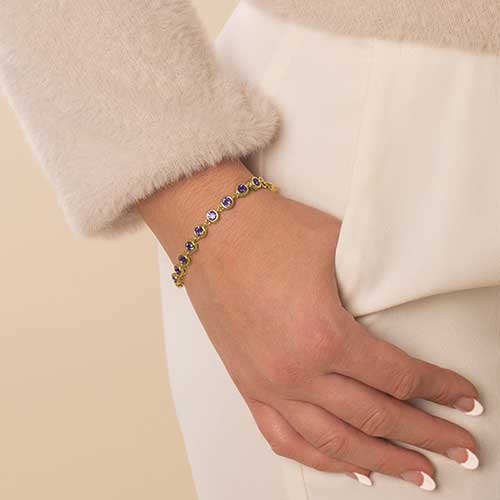 Woman wearing 12k gold plated chain with round, bezel set amethyst cubic zirconia crystals.