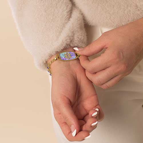 Woman wearing gold tone stainless steel lilac abalone medical ID tag with gold tone medical symbol.