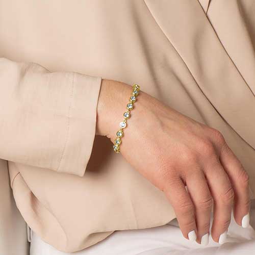 Woman wearing a bracelet featuring individually linked, round, aquamarine cubic zirconias