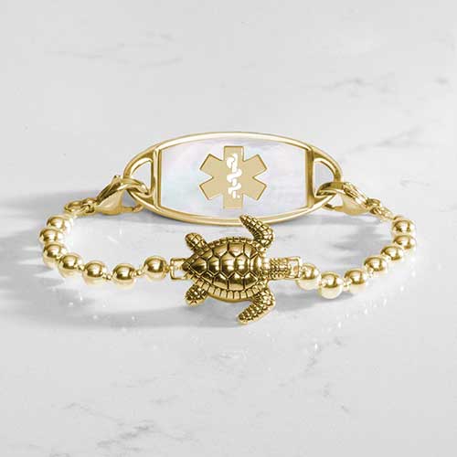 Gold tone beaded bracelet featuring a sea turtle centerpiece, attached to a gold tone medical ID with mother of pearl inlay.
