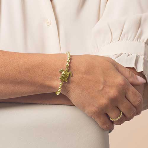 Model wearing a gold tone beaded bracelet with sea turtle centerpiece.
