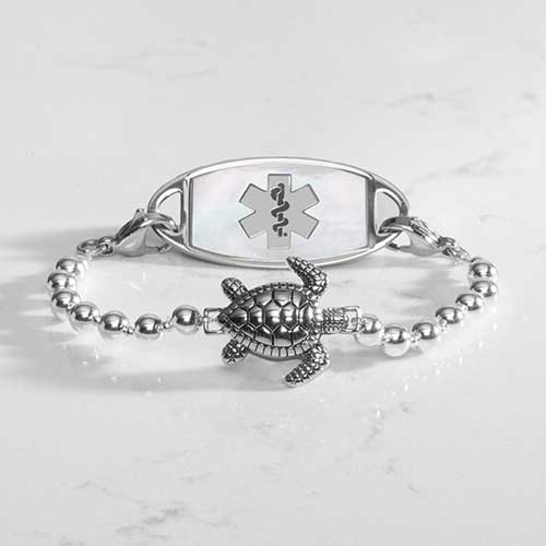 Silver beaded bracelet featuring a sea turtle centerpiece, attached to a stainless steel medical ID with mother of pearl inlay.