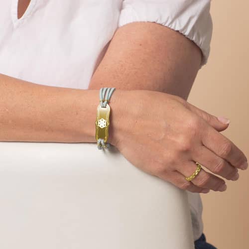 Woman wearing Avery SmartSize Medical ID Bracelet with suede light blue tone leather band and adjustable chain with a Gold La Petite tag with a white Cadeusus 