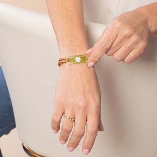 Woman wearing Avery SmartSize Medical ID Bracelet with suede copper tone leather band and adjustable chain with a Gold La Petite tag with a white Cadeusus 