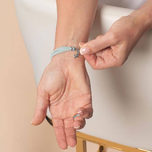 Woman adjusting the clasp of a light blue wrap-style medical ID bracelet, highlighting the secure closure and comfortable fit.